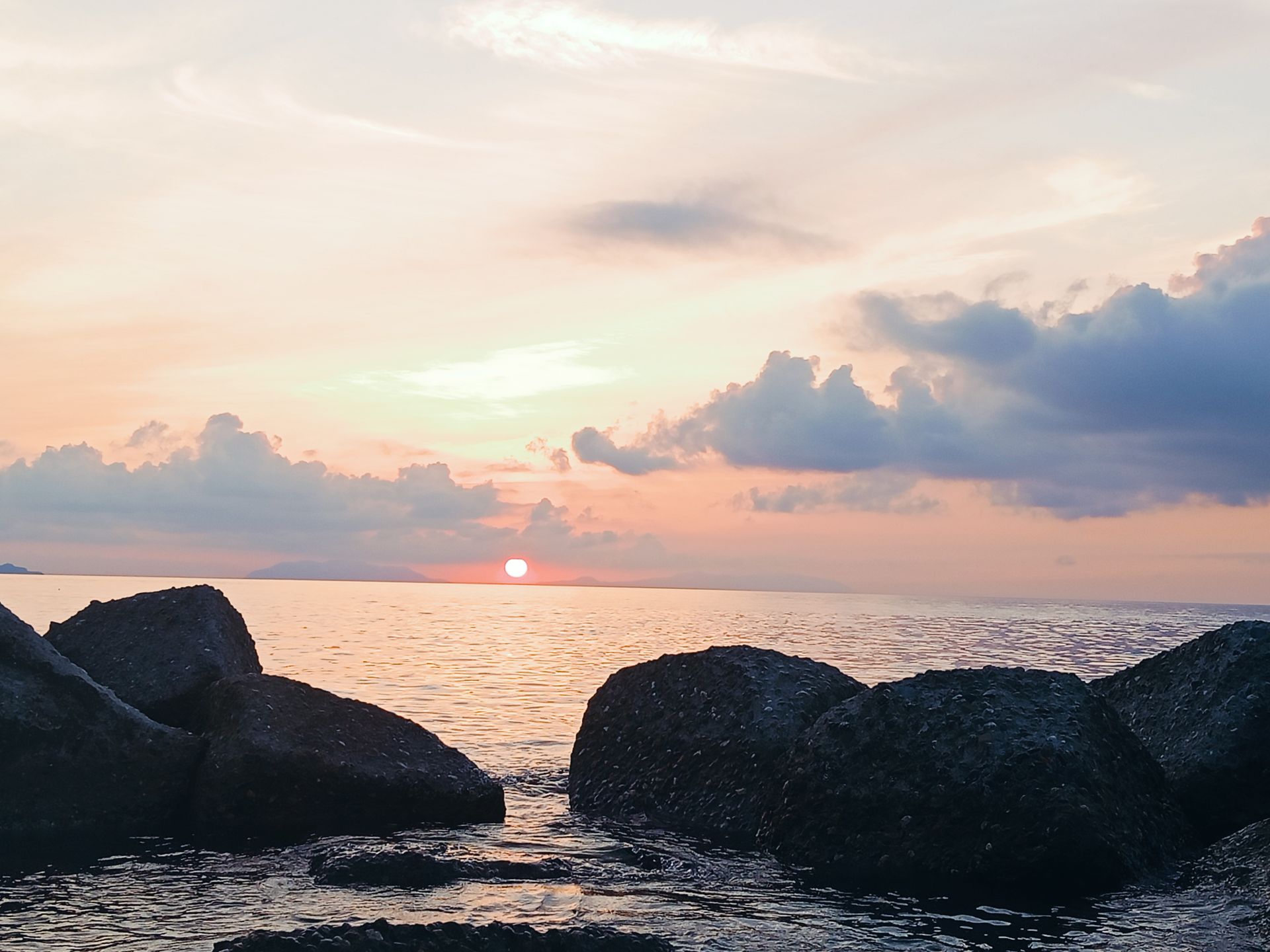 Tramonto sul mare di Sicilia tra gli scogli, con le isole all'orizzonte